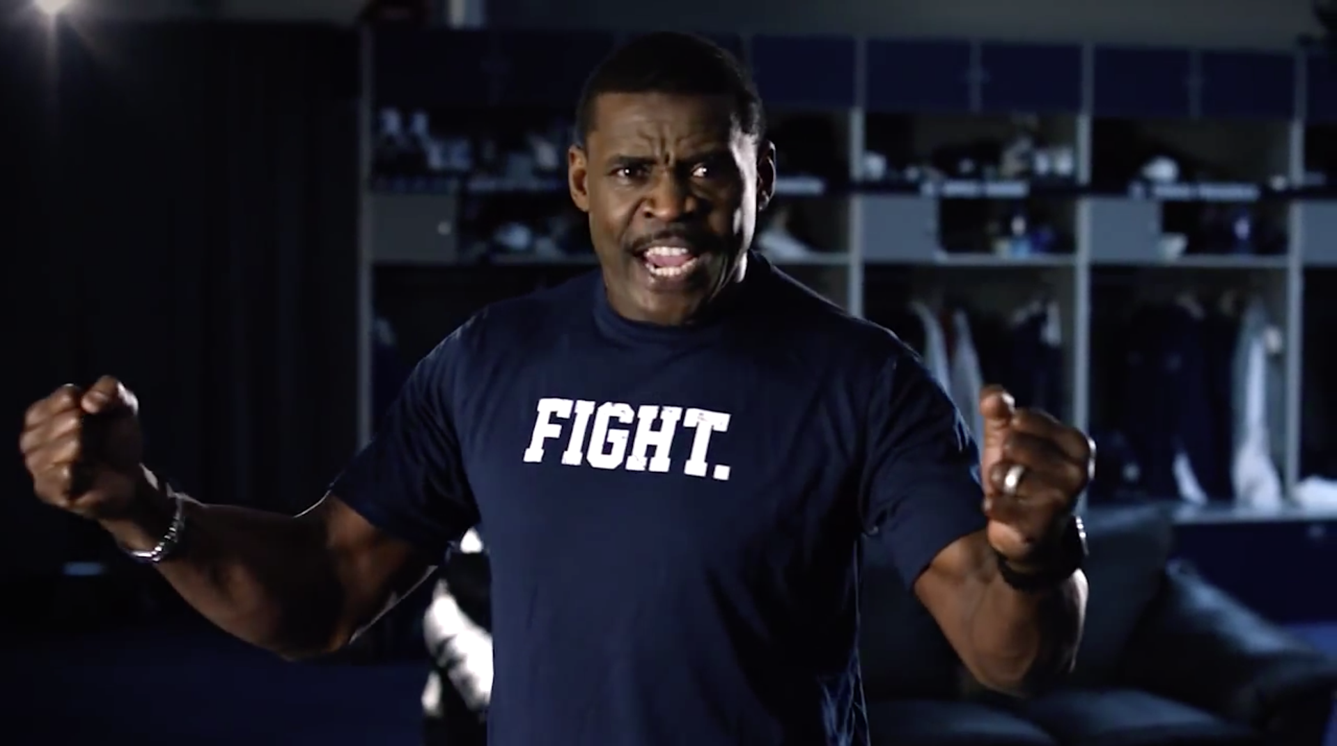 A man wearing a Dallas Cowboys navy blue shirt that reads "FIGHT" stands with his arms out like he is giving an impassioned speech - from Red Productions, a full service film & production company in Fort Worth Texas